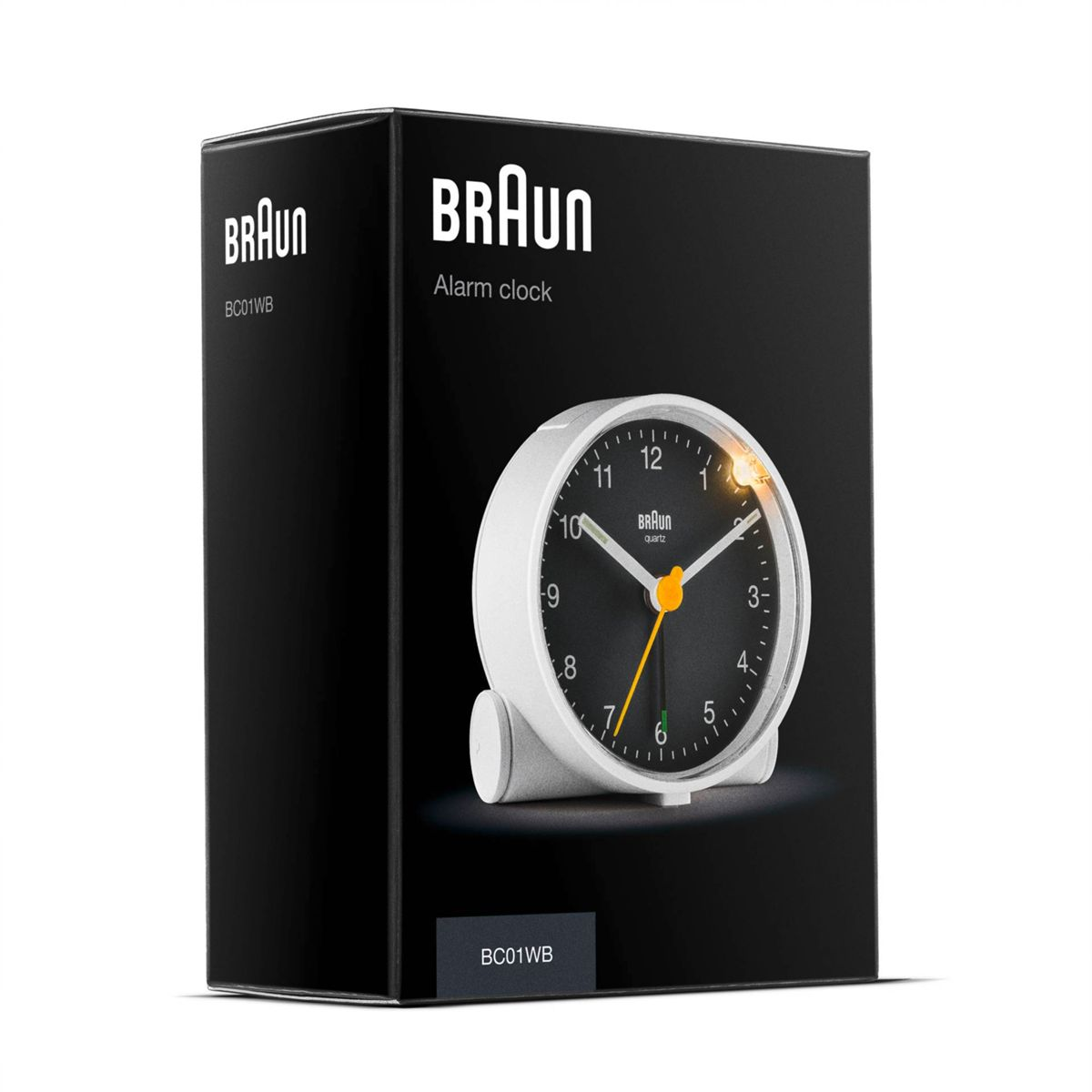Schwarze Verpackung mit einem weißen Braun Wecker mit schwarzem Zifferblatt und gelben Akzenten.