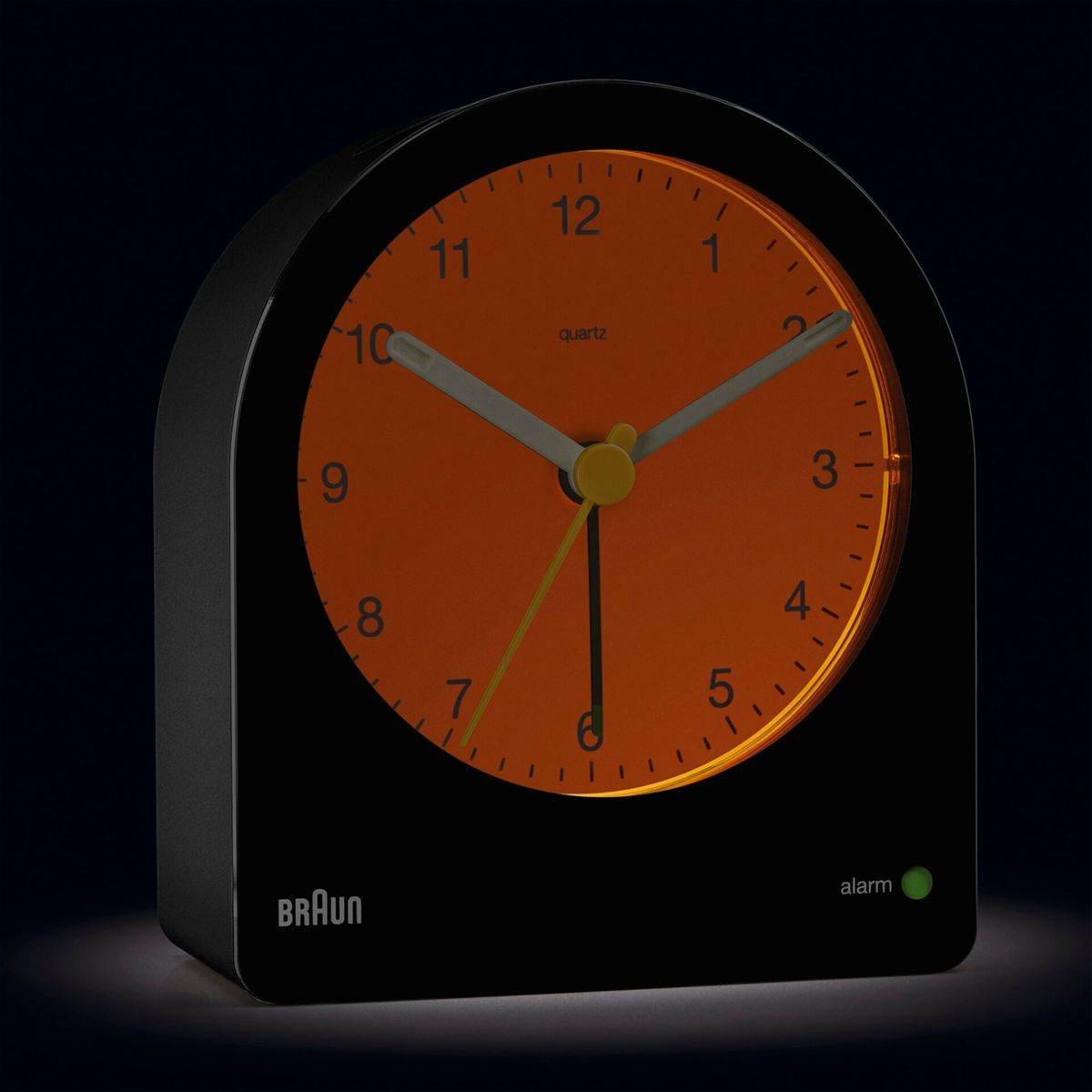 Un despertador Braun negro con esfera naranja y manecillas luminosas.