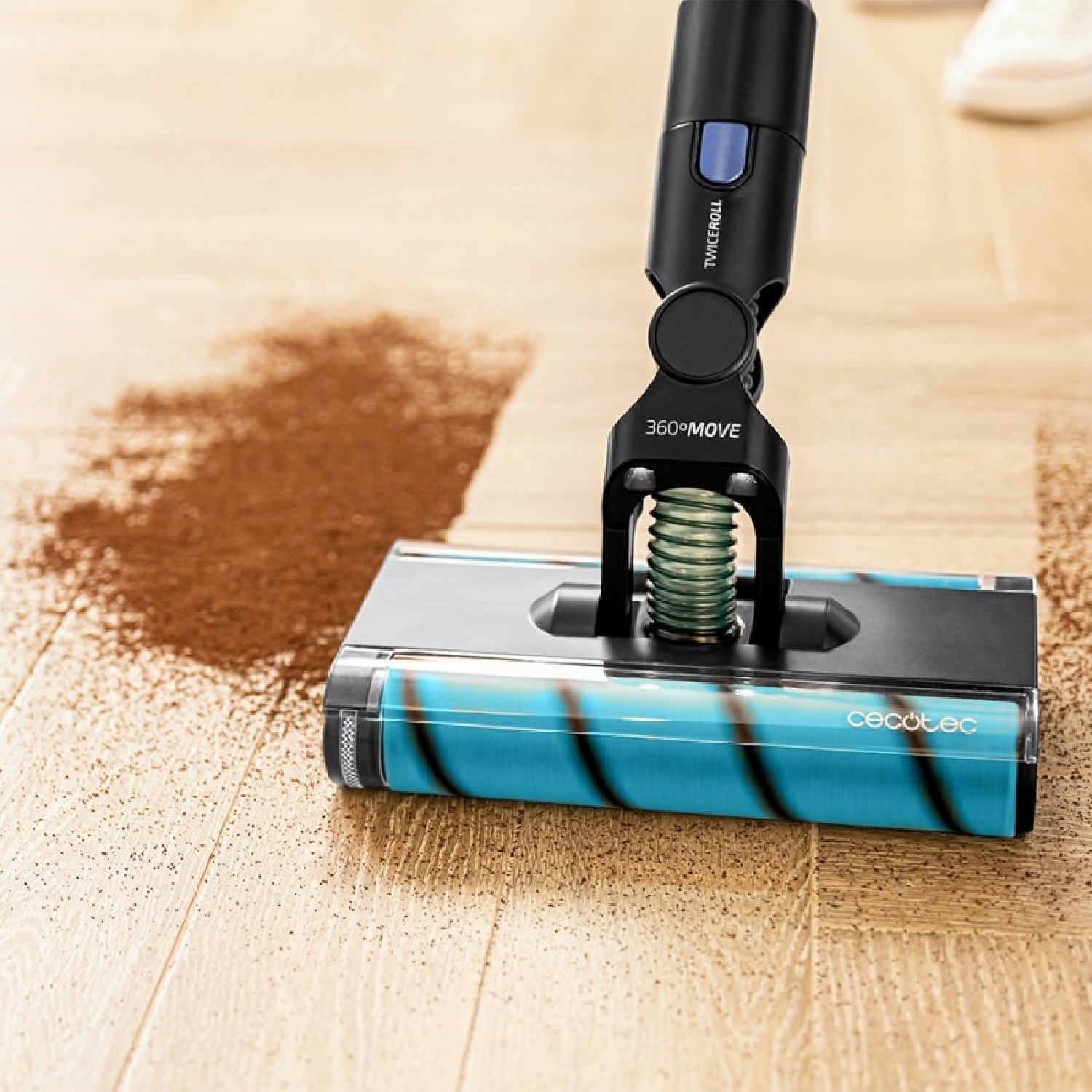 Un cabezal de aspiradora con cepillo azul limpia posos de café de un suelo de madera.
