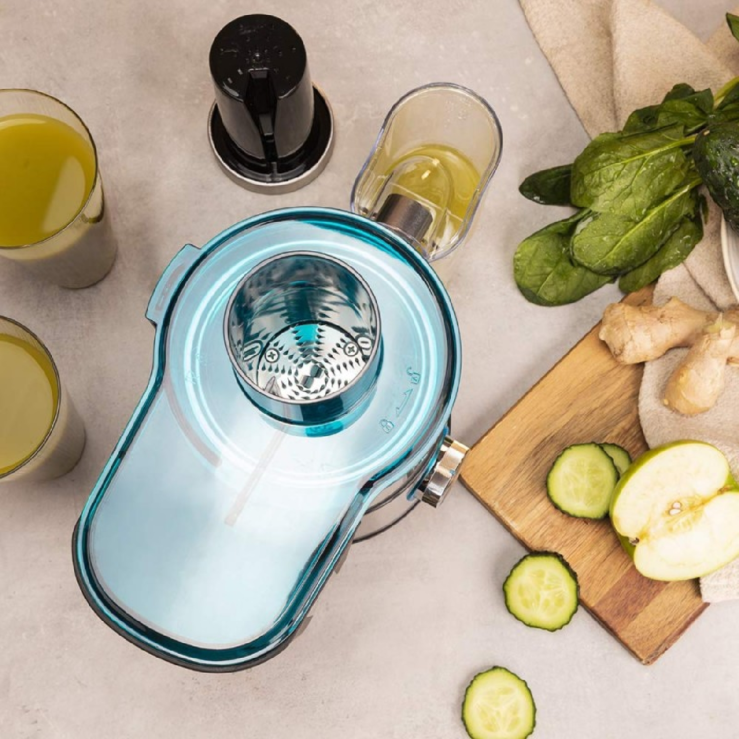Un estrattore blu con bicchieri di succo, fette di cetriolo, mela, spinaci e zenzero.