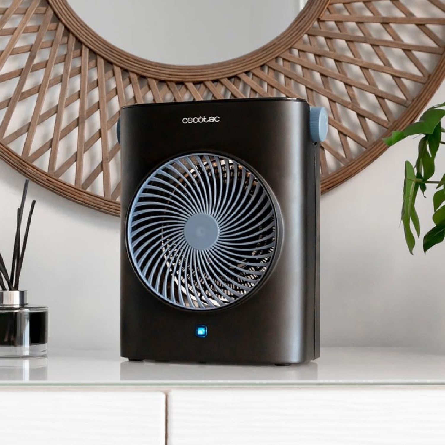 Un ventilador negro con rejilla azul está sobre un estante blanco.