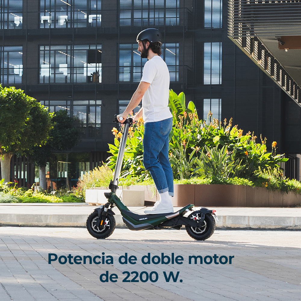 Hombre monta patinete eléctrico frente a edificio moderno con plantas.