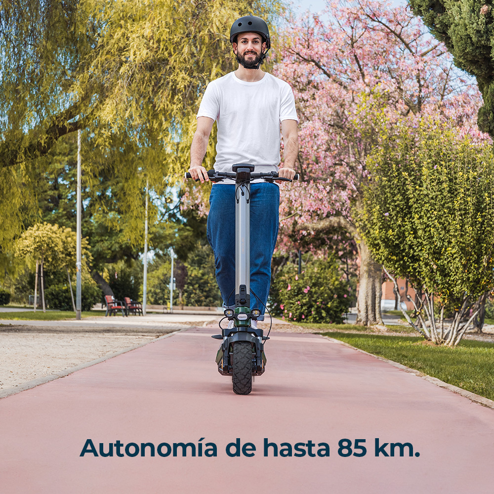 Un hombre monta un patinete eléctrico por un sendero del parque, rodeado de árboles y arbustos.
