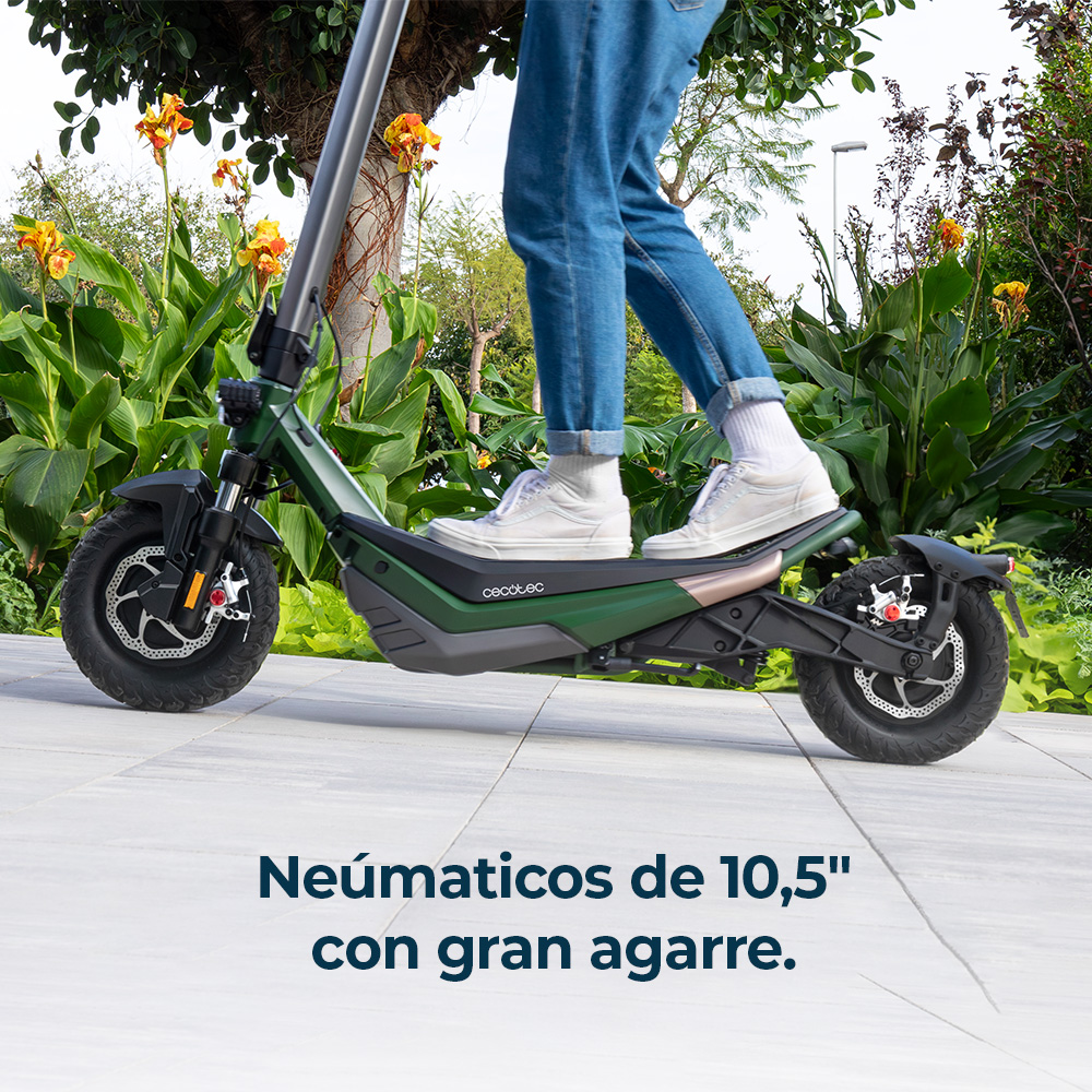 Persona en patinete eléctrico verde con zapatillas blancas y vaqueros, al aire libre.