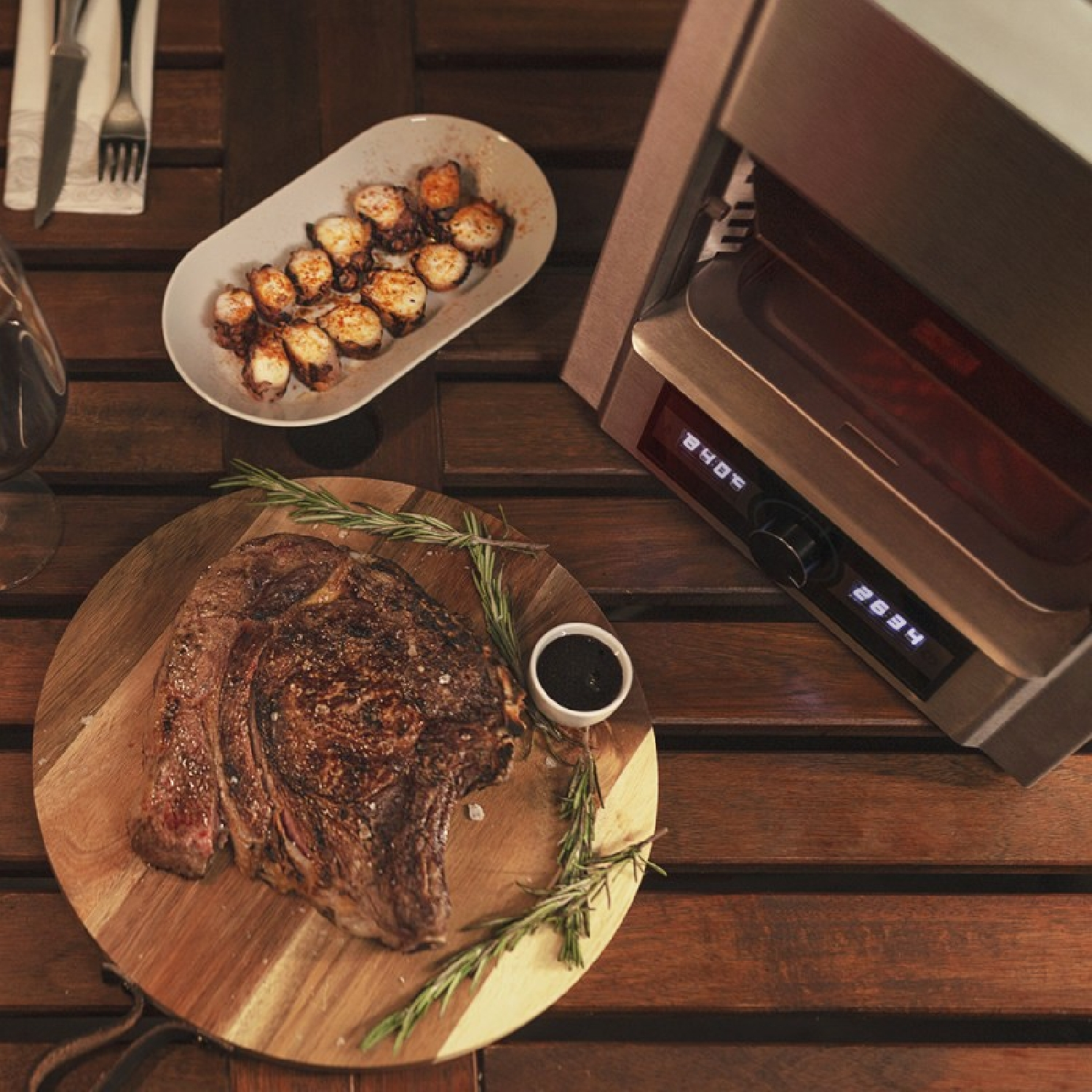Grande bistecca, polpo e dispositivo di cottura su tavolo di legno.