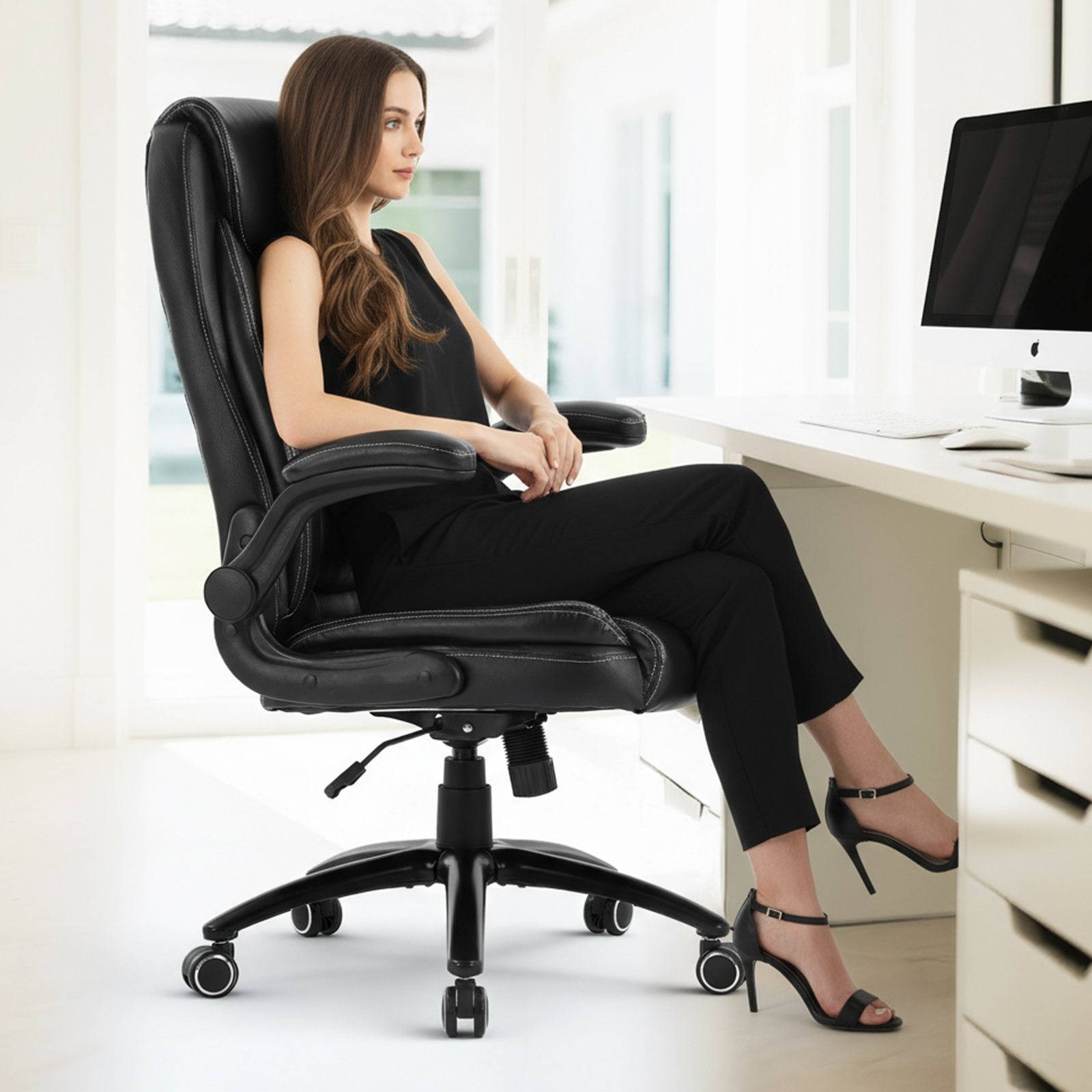 Una mujer se sienta en una silla de oficina negra en un escritorio con una computadora.