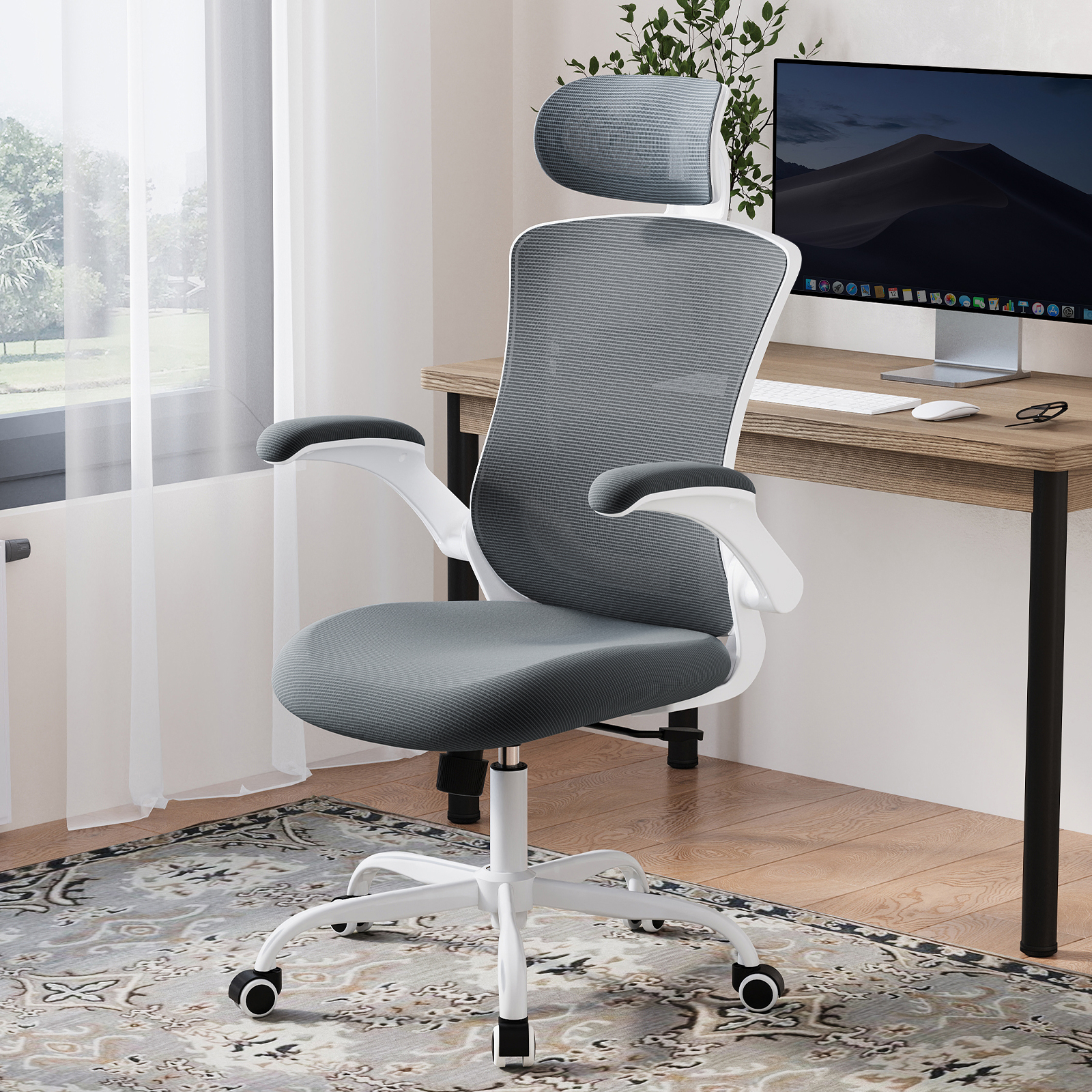 Una silla de oficina gris con base blanca sobre alfombra, delante de un escritorio con ordenador.
