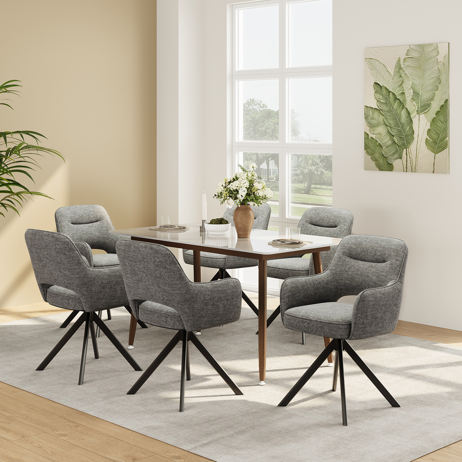 Una sala da pranzo con tavolo in legno, quattro sedie grigie, vaso con fiori e quadro di foglie.