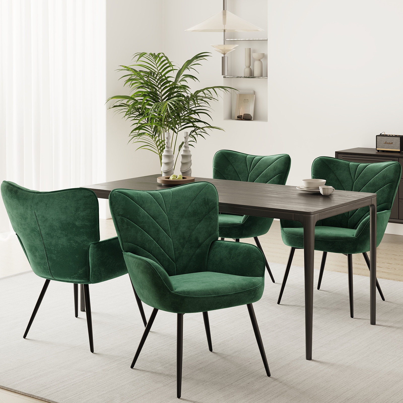 Ein Esszimmer mit einem dunklen Holztisch, vier grünen Samtstühlen und einer Palme.