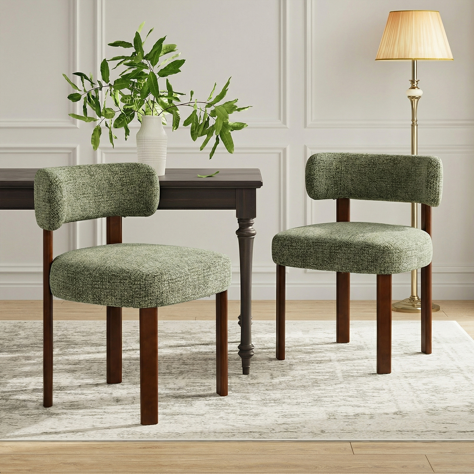 Due sedie verdi imbottite con gambe in legno accanto a un tavolo in legno scuro con un vaso di foglie verdi.