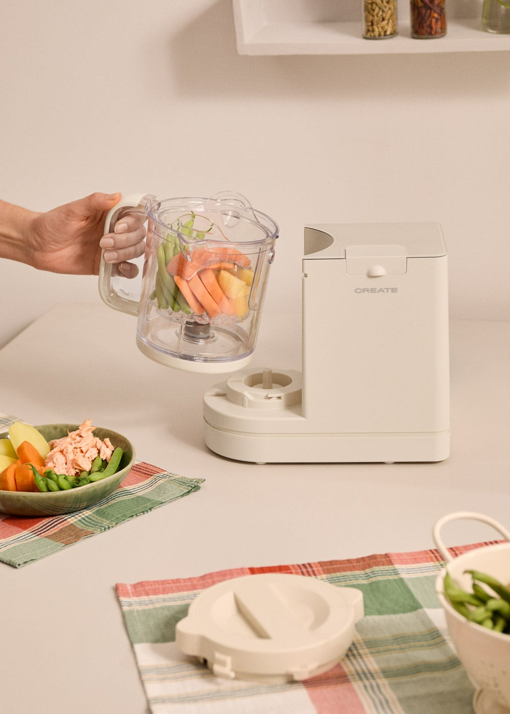 Mano sostiene jarra de licuadora con verduras; cuenco con pescado y verduras cerca.