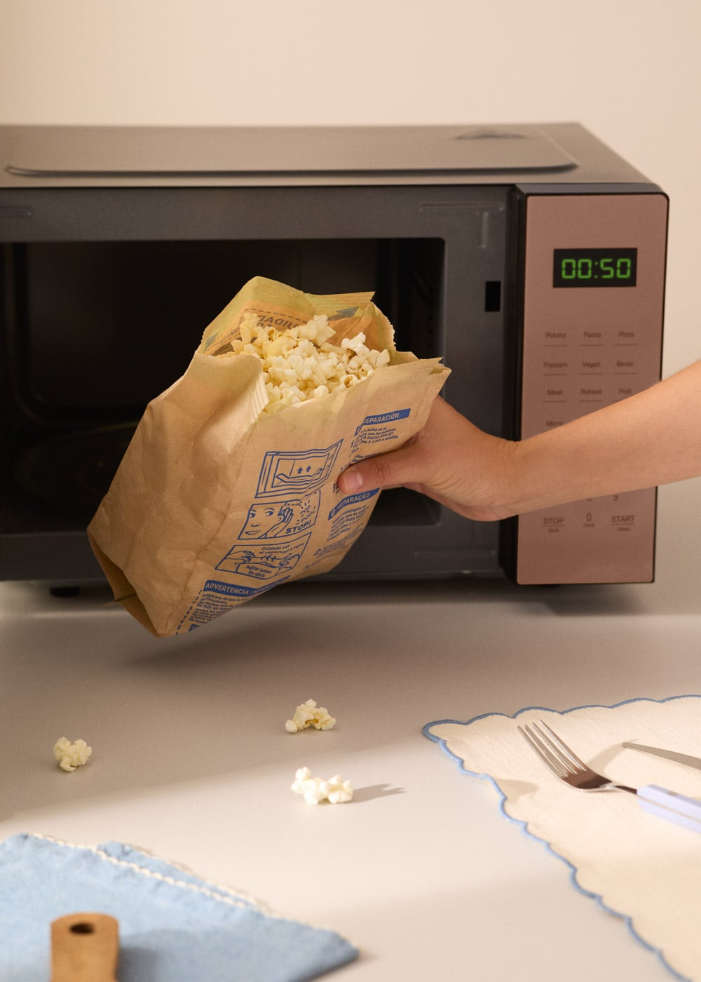 Una mano sostiene una bolsa de papel llena de palomitas junto a un microondas abierto.