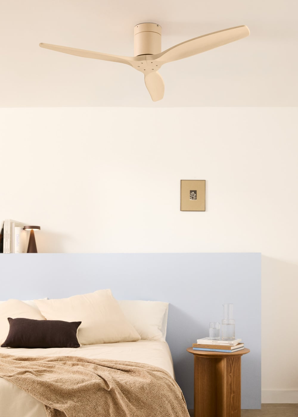 Un ventilador de techo beige sobre una cama con cabecero azul claro y mesita de noche.