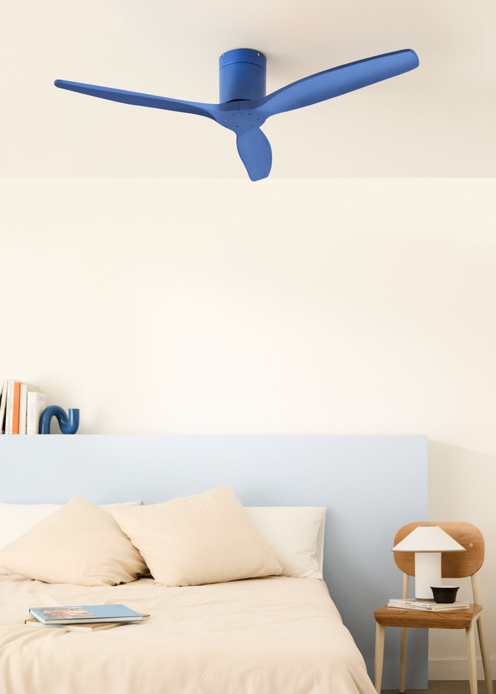 Un ventilador de techo azul sobre una cama con almohadas beige y libros.