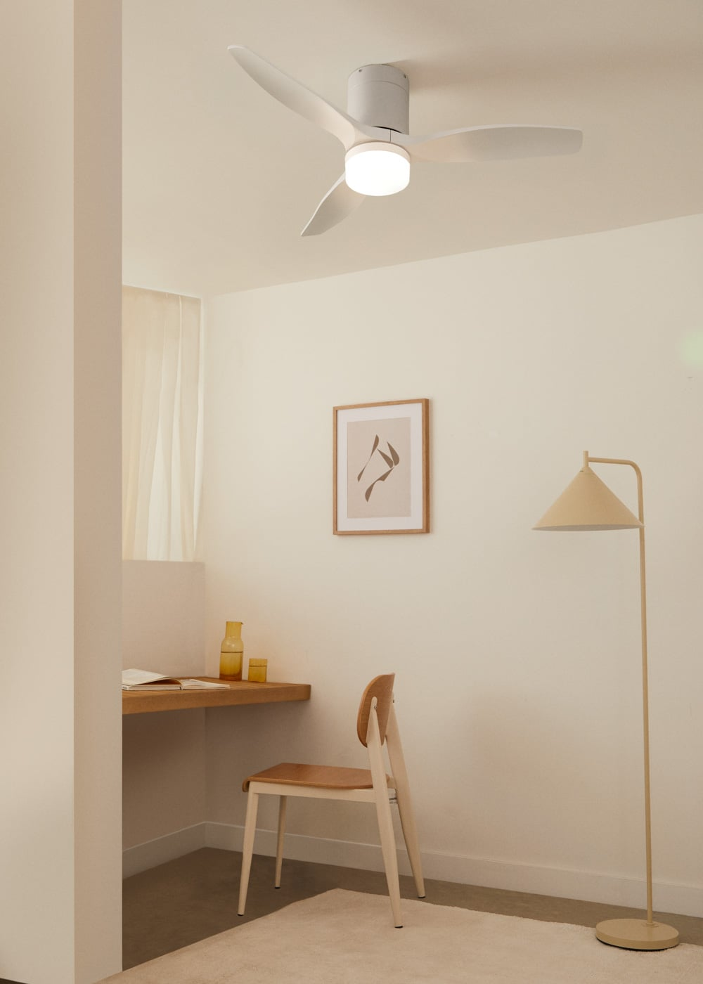 Una habitación minimalista con escritorio, silla, lámpara de pie y ventilador de techo.