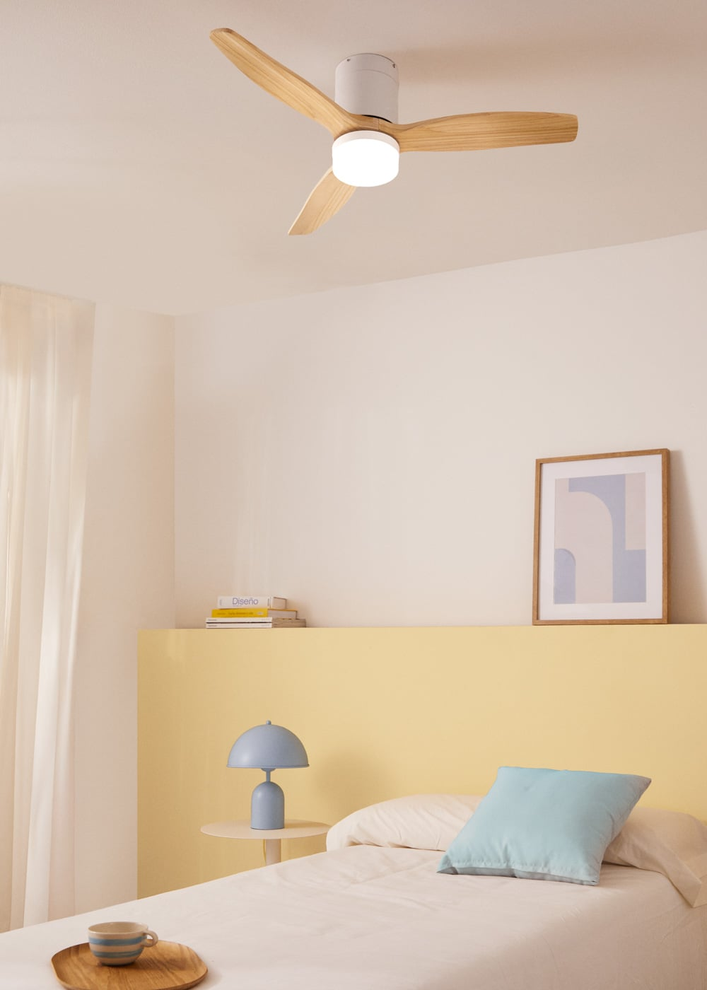 Ventilador de techo con luz sobre una cama con almohadas y lámpara de noche.