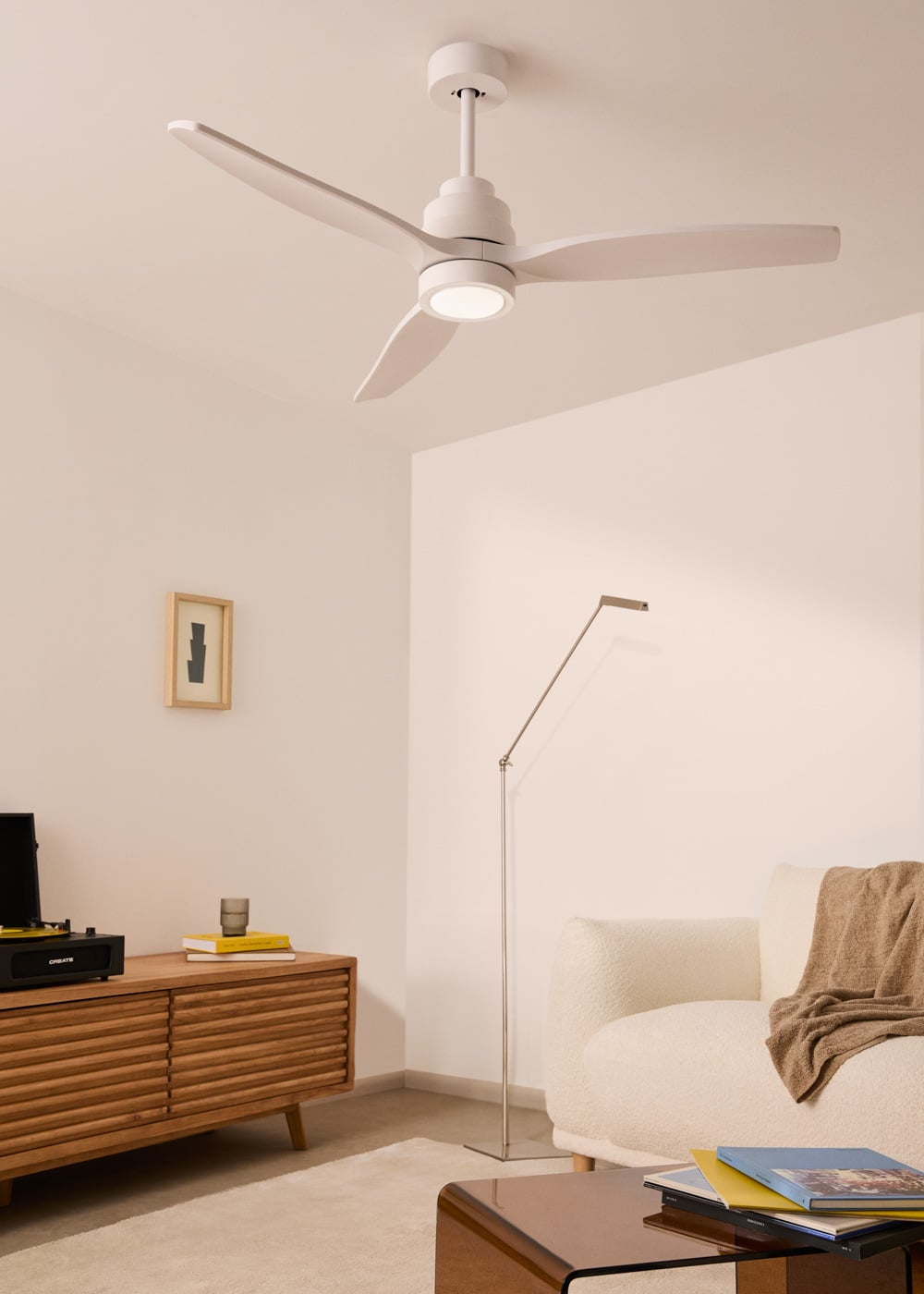 Un ventilador de techo blanco con luz sobre una consola multimedia de madera y un sofá texturizado.