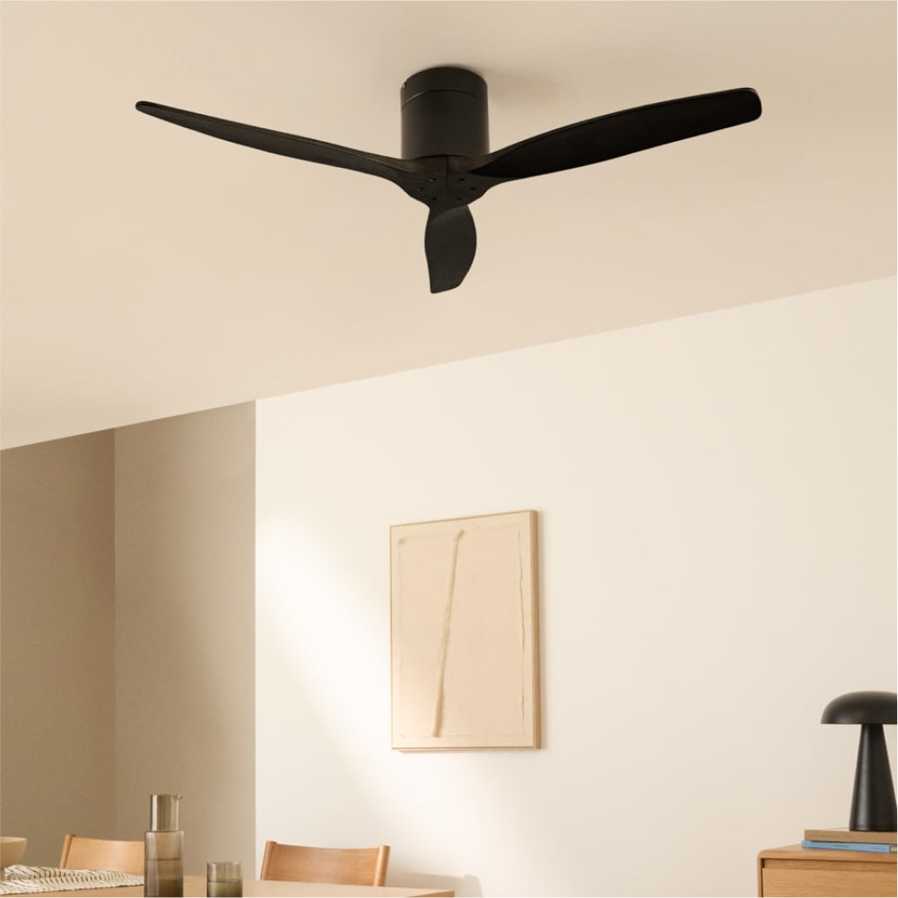 Un ventilador de techo negro de tres aspas sobre un comedor con arte minimalista.