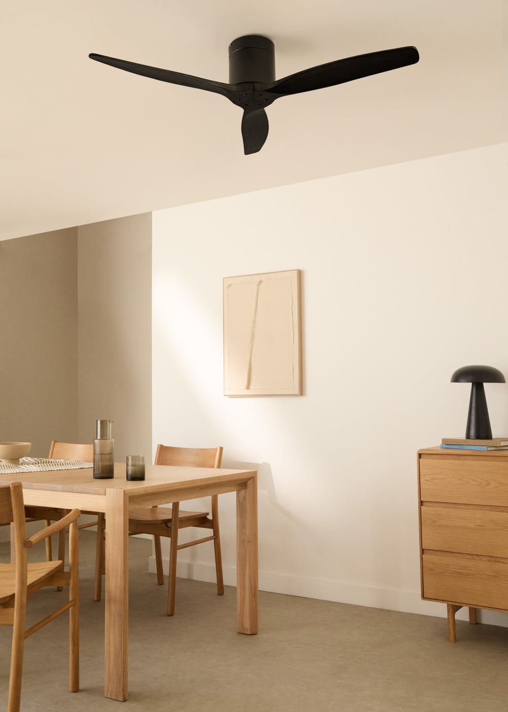 Ventilador de techo negro sobre mesa de madera con sillas. Arte de pared beige.
