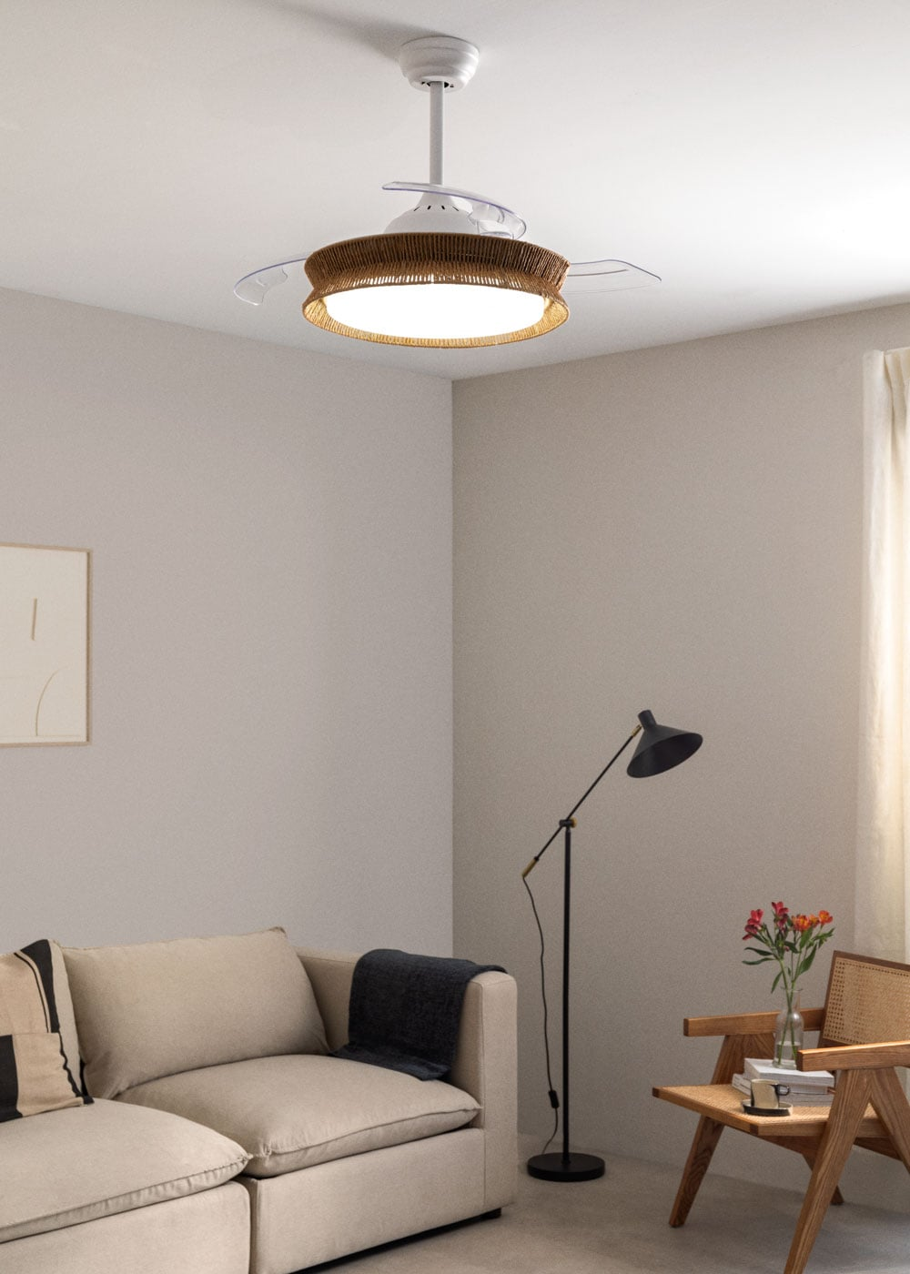 Un ventilador de techo con borde de ratán sobre un sofá beige, con una silla al lado.