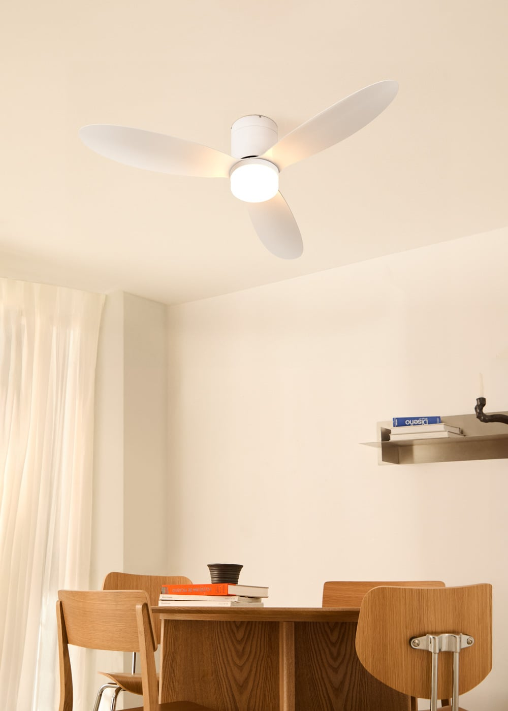 Un ventilador de techo blanco con luz está sobre una mesa de madera con sillas.