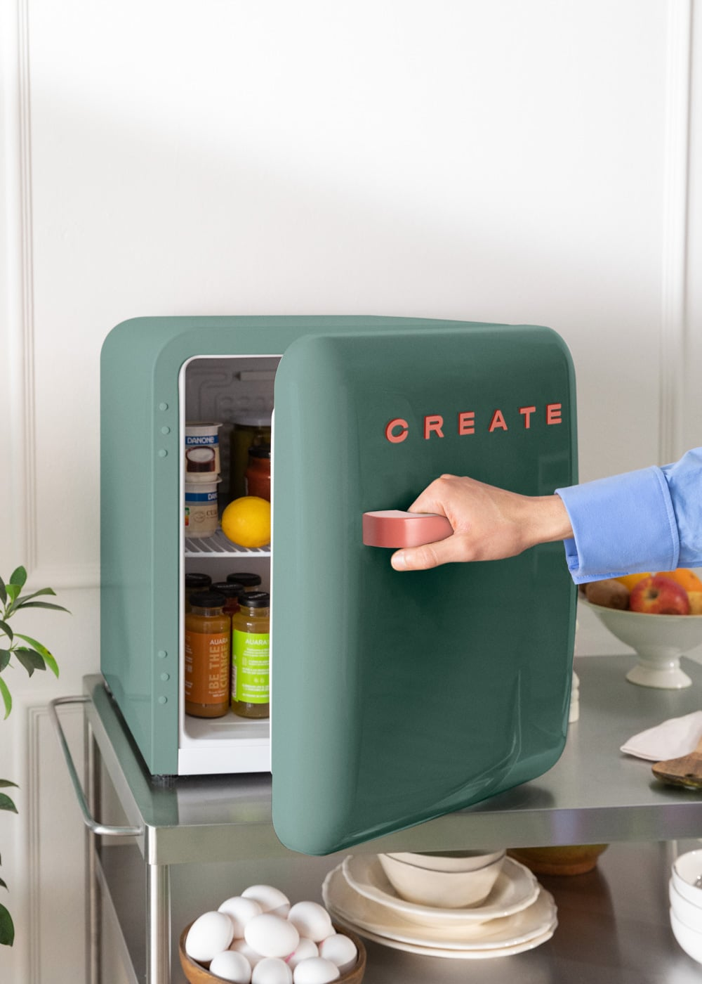 Un refrigerador verde con la puerta abierta, lleno de comida. Una mano alcanza el tirador.