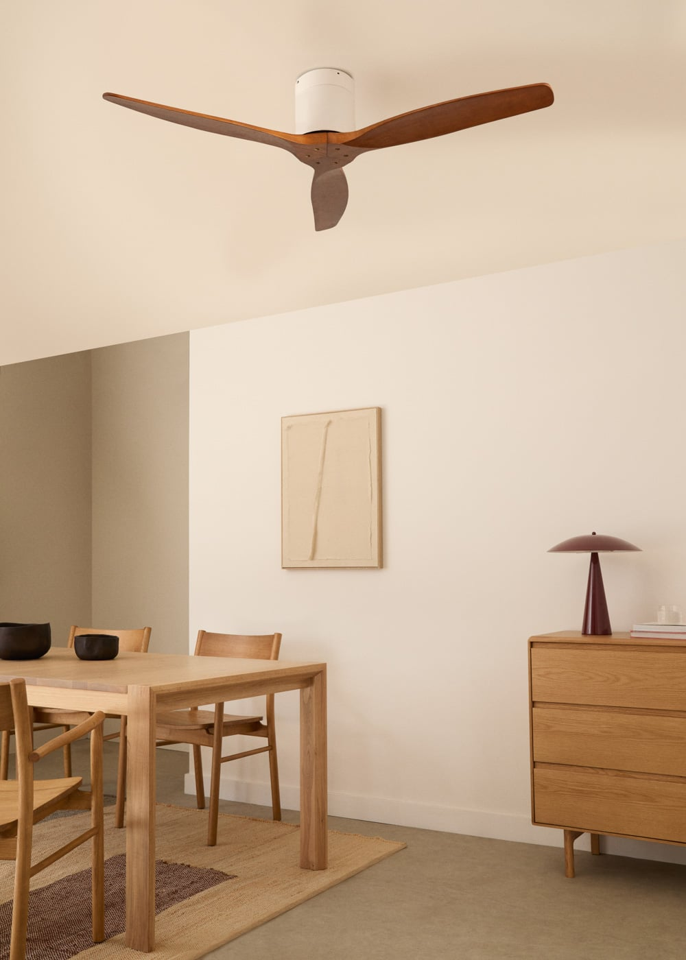 Un comedor con mesa de madera, sillas, ventilador de techo y cómoda.