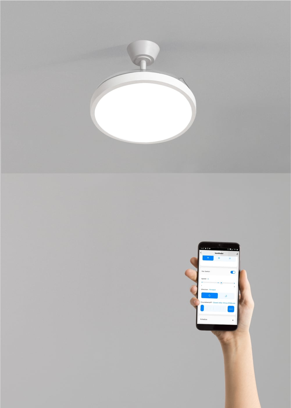 Se muestra un ventilador de techo blanco con luz, con una mano sosteniendo un teléfono con controles.