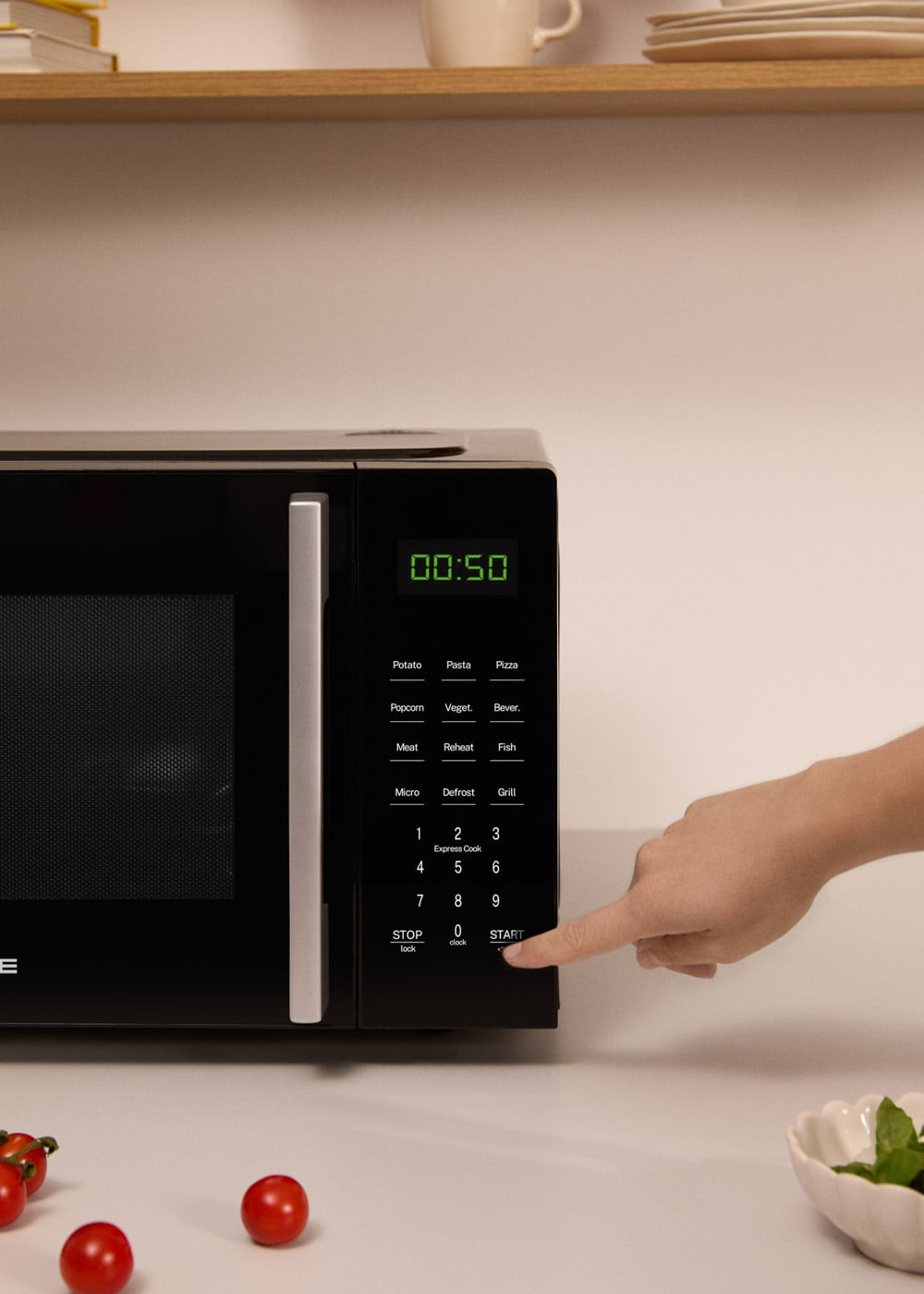 Una mano presiona el botón de inicio en un microondas negro con pantalla digital iluminada.
