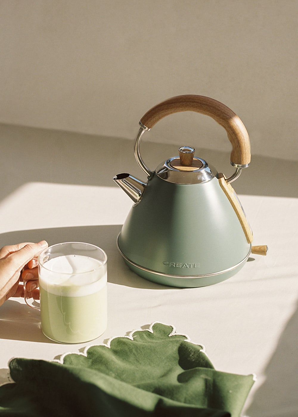 Un hervidor verde con mango de madera junto a un vaso de leche.