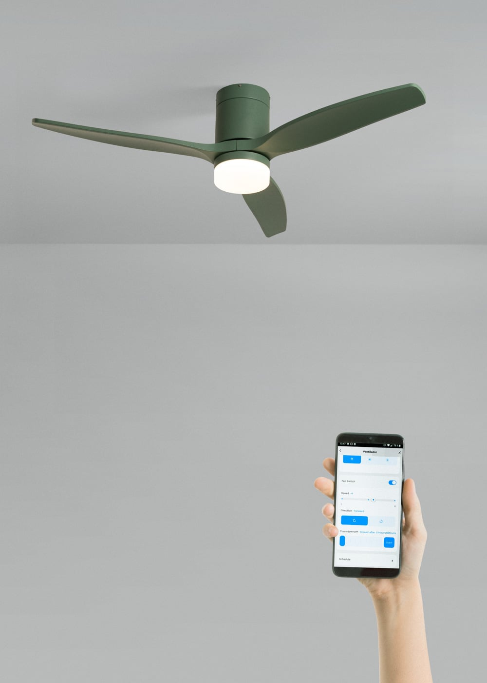 Un ventilador de techo verde con luz es controlado por una mano que sostiene un smartphone con controles.