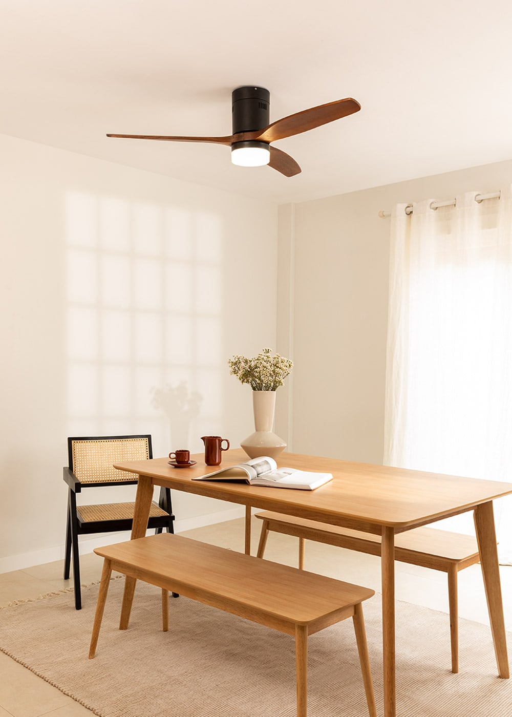 Un comedor con mesa de madera, banco, silla, jarrón y ventilador de techo.