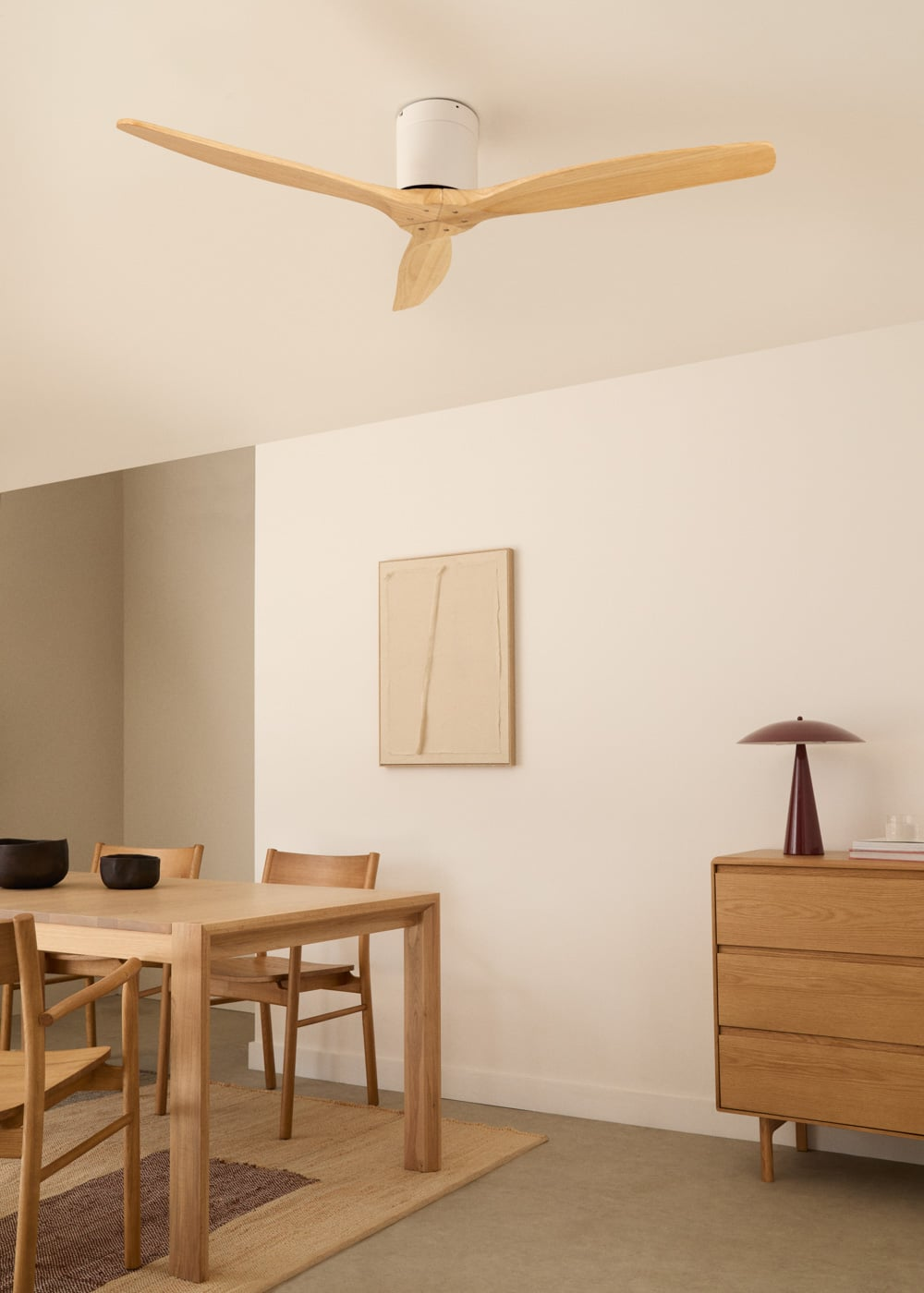 Mesa de madera con sillas, ventilador de techo, cuadro y cómoda con lámpara.