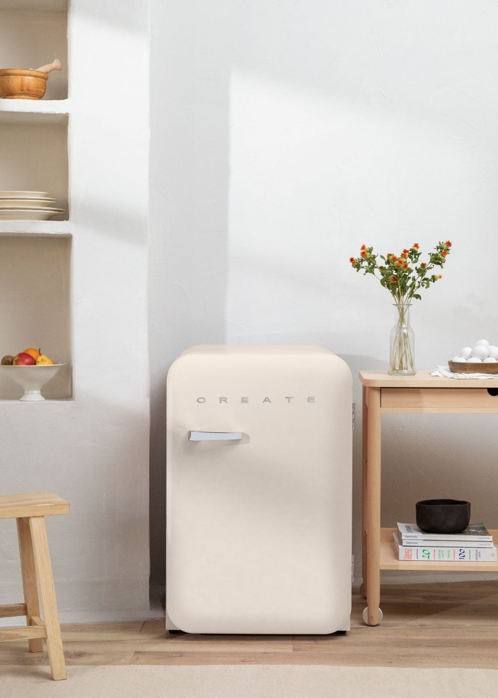 Un refrigerador color crema con la palabra CREATE se encuentra junto a una mesa de madera con flores.