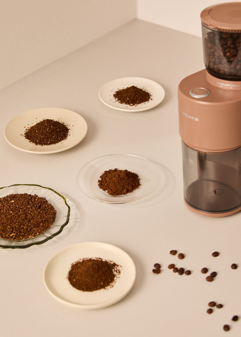 Un molinillo de café rosa con granos y café molido en platos.