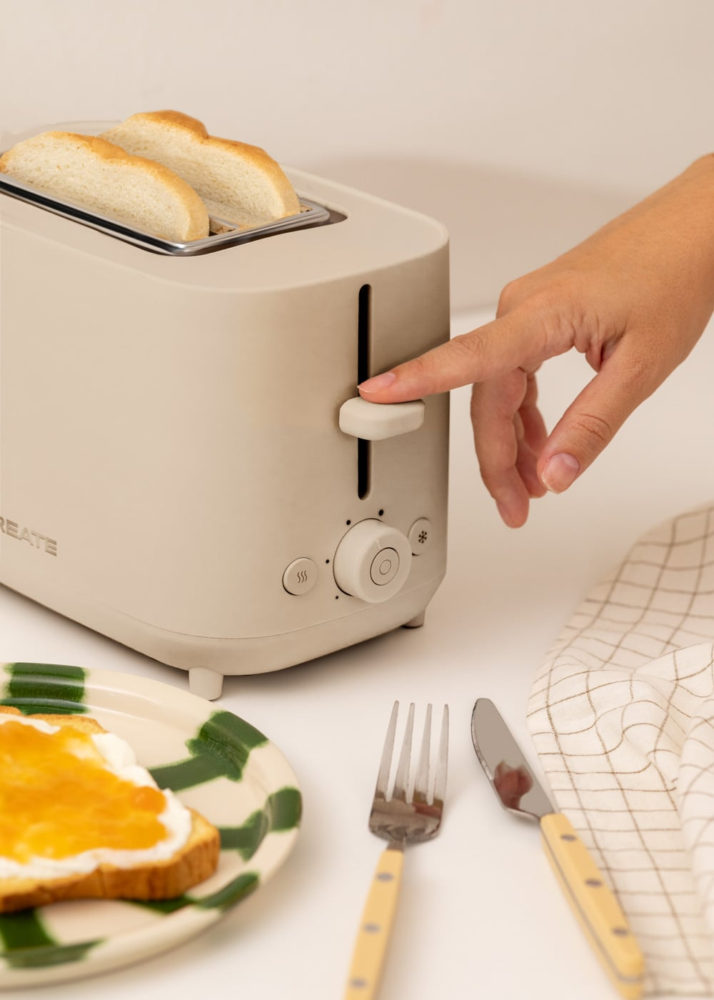 Una mano presiona la palanca de una tostadora beige con dos rebanadas de pan.