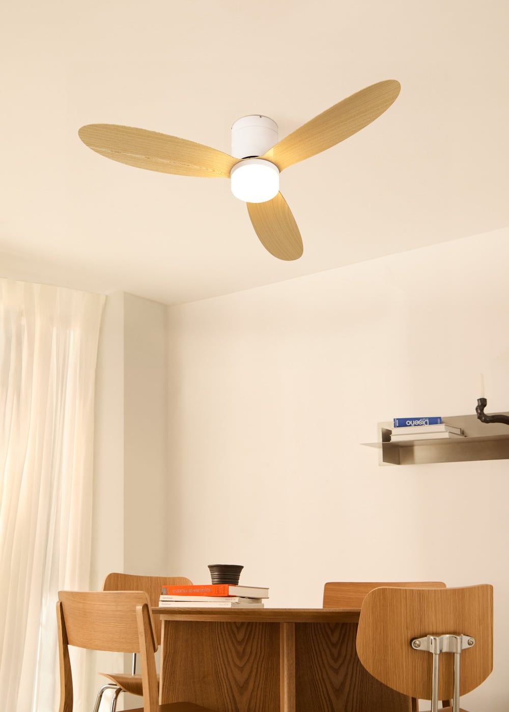 Un ventilador de techo con aspas de madera y luz sobre una mesa de madera con sillas.