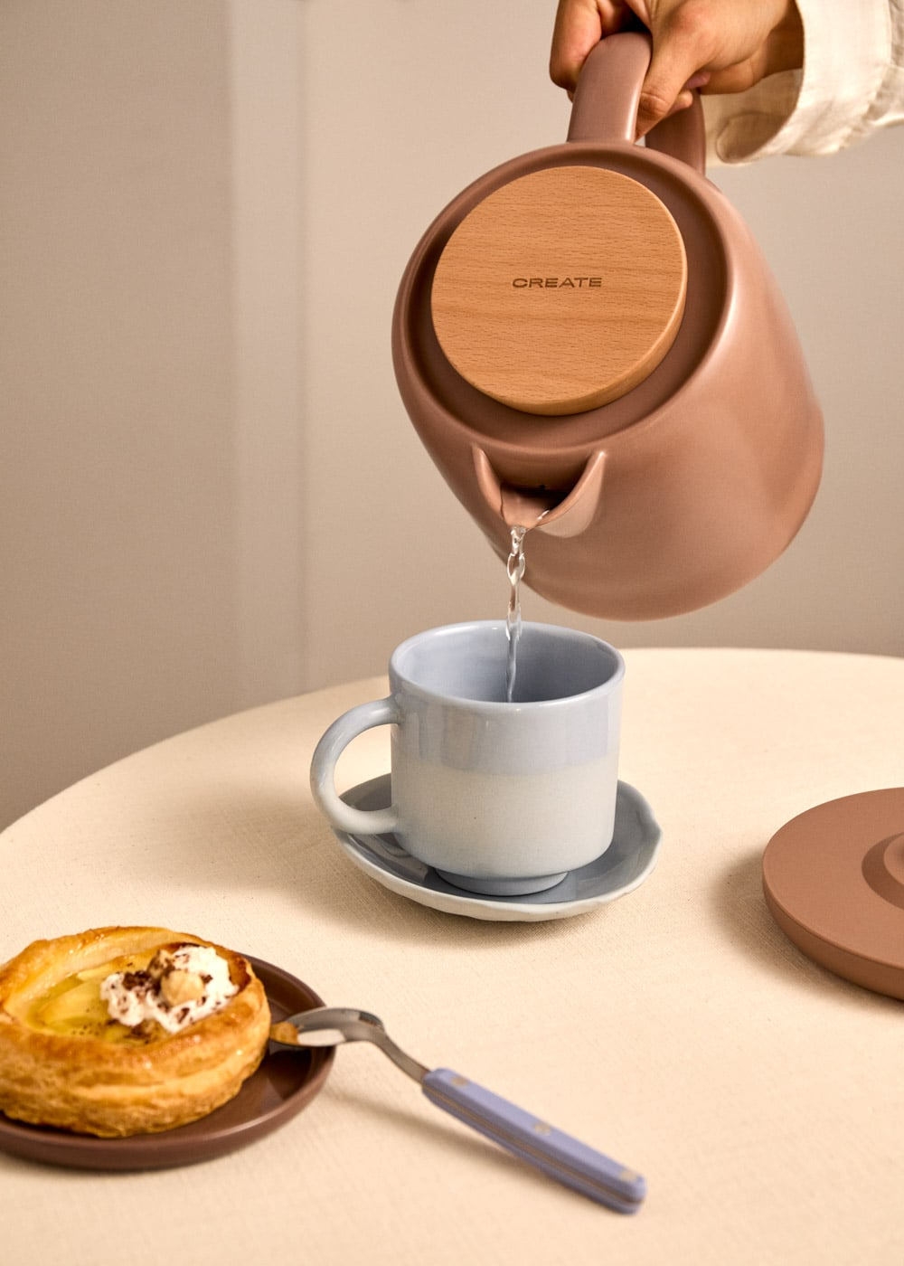 Una mano vierte agua de una tetera en una taza. Un pastel está cerca.