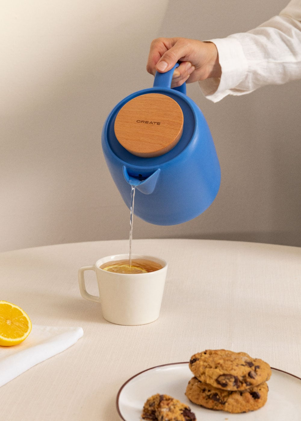 Una mano vierte agua de una jarra azul en una taza con rodajas de limón.