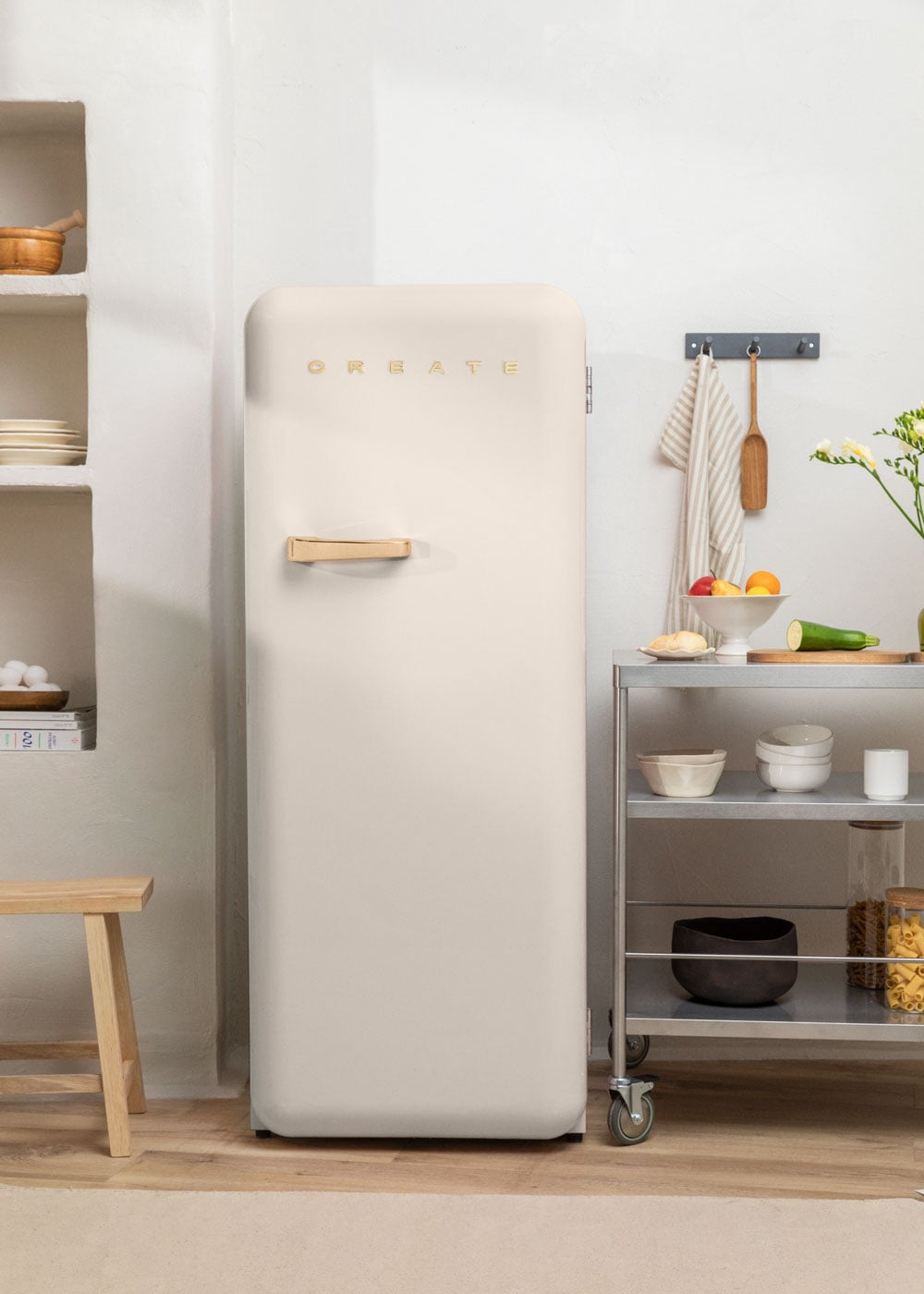 Refrigerador color crema con tirador de madera, junto a un carrito rodante con alimentos.