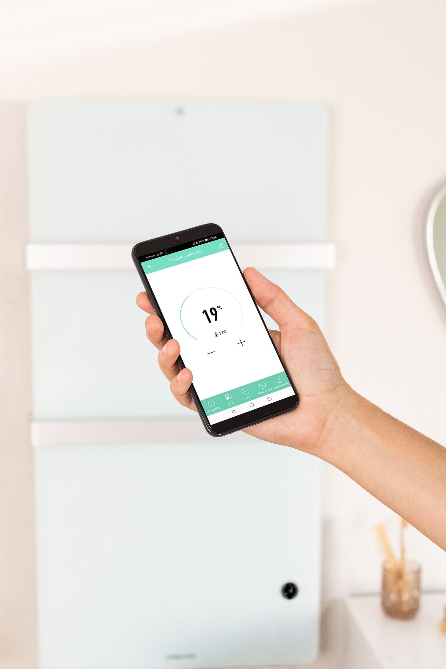 Una mano sostiene un smartphone que muestra una app para controlar un toallero eléctrico.