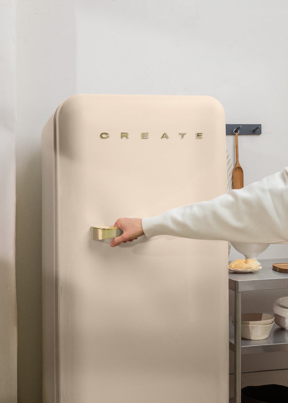 Una mano abre un refrigerador color crema con un asa dorada. "CREATE" está escrito arriba.