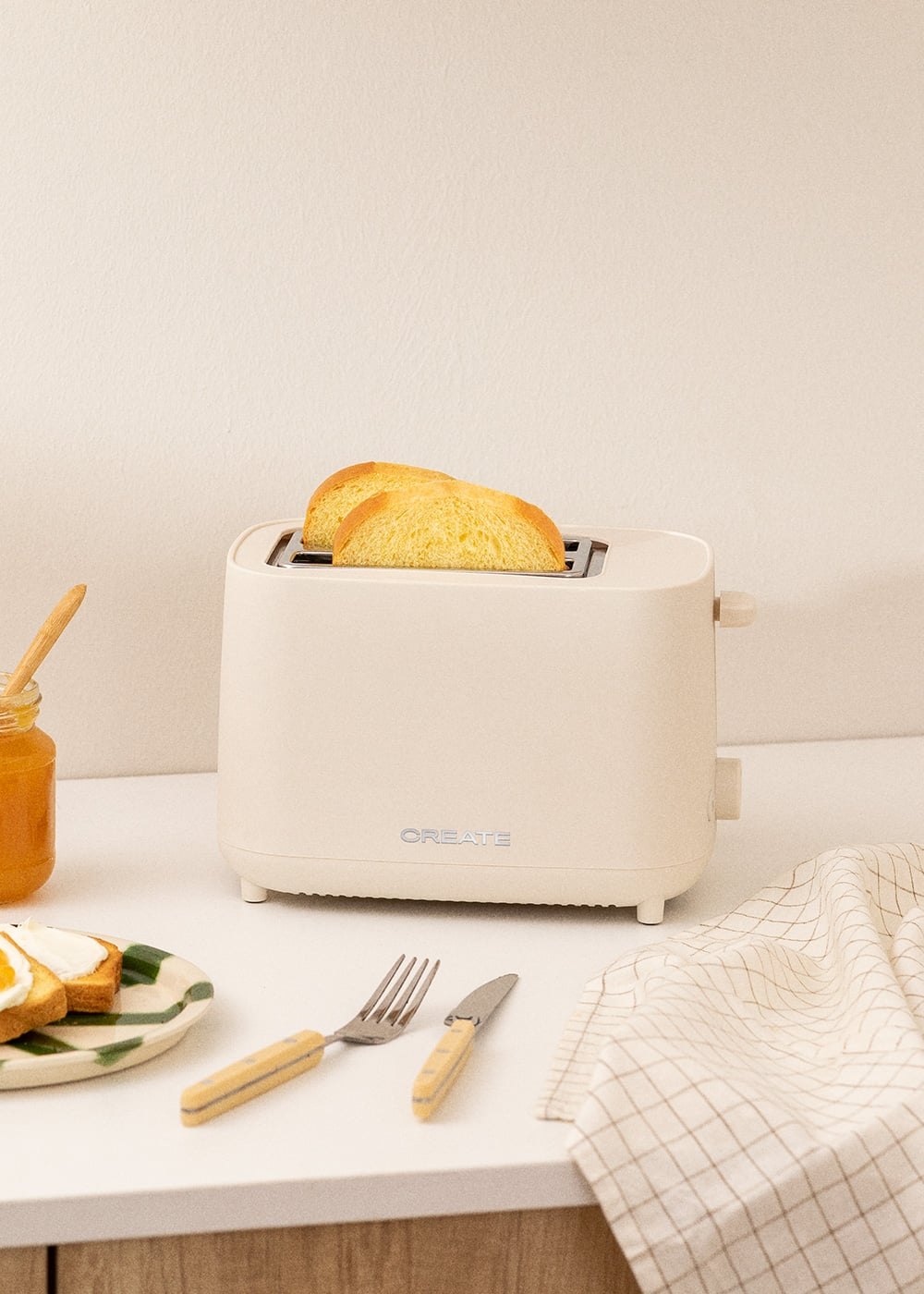 Un grille-pain de couleur crème avec deux tranches de pain grillé, à côté un pot de confiture et une assiette.