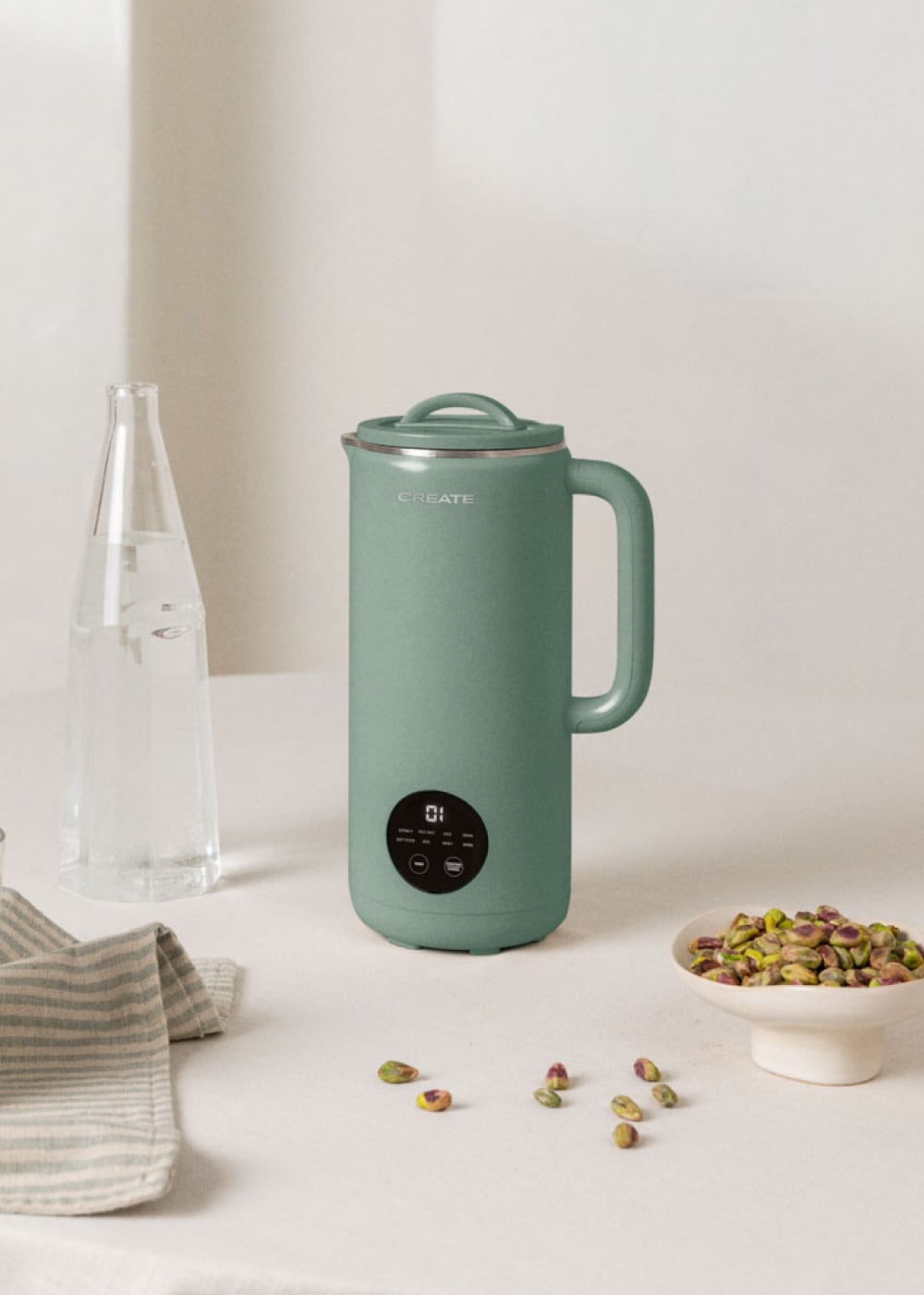 Una jarra verde CREATE con pantalla digital junto a una botella de vidrio y un bol de pistachos.
