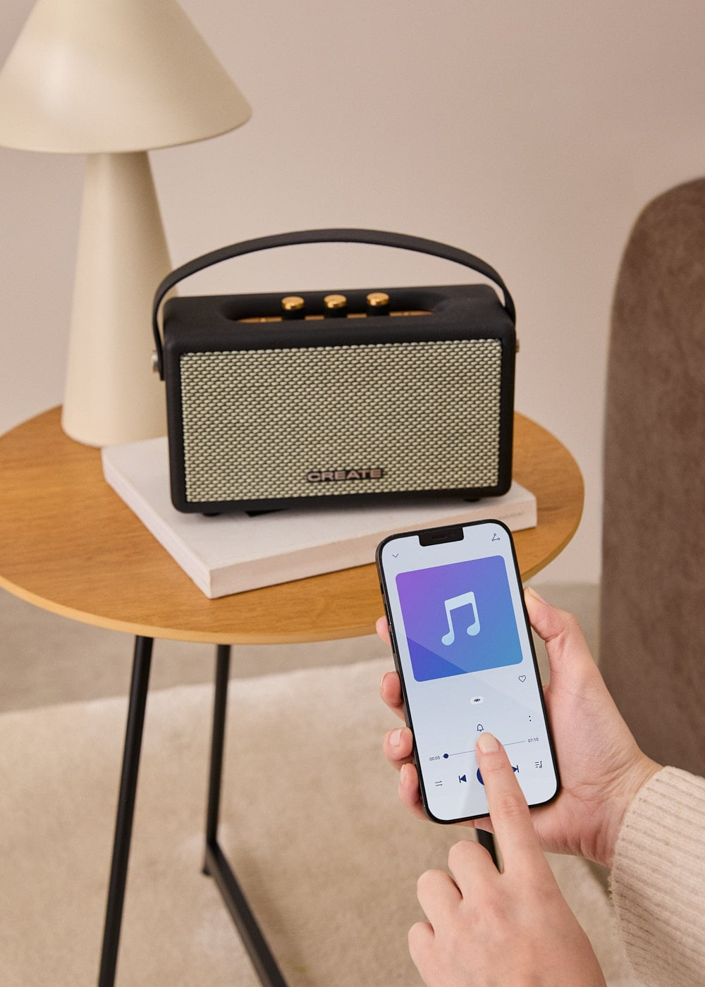 Persona usando aplicación de música en smartphone junto a altavoz negro en mesa.