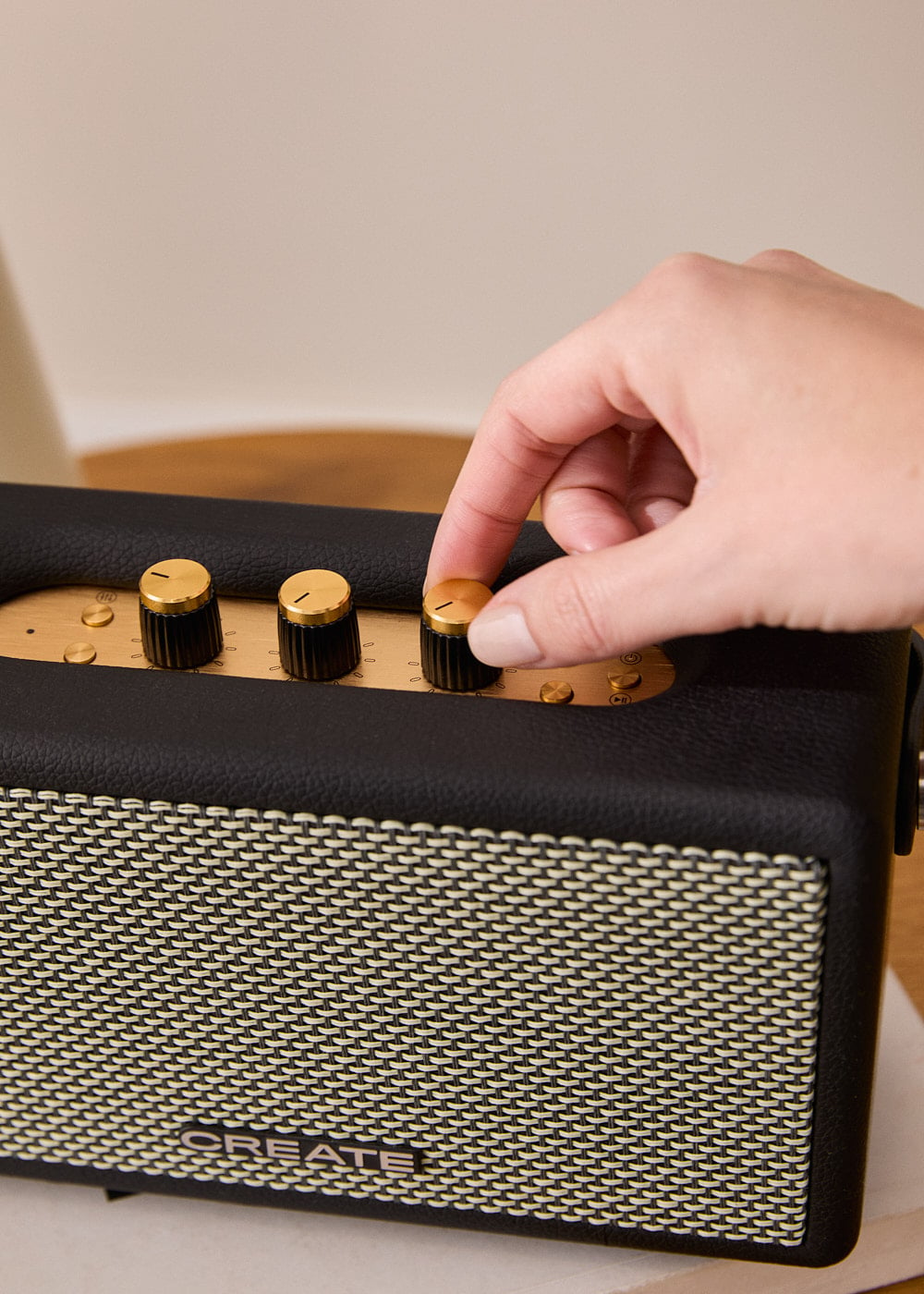 Una mano gira un mando dorado en un altavoz negro con frontal de tela.