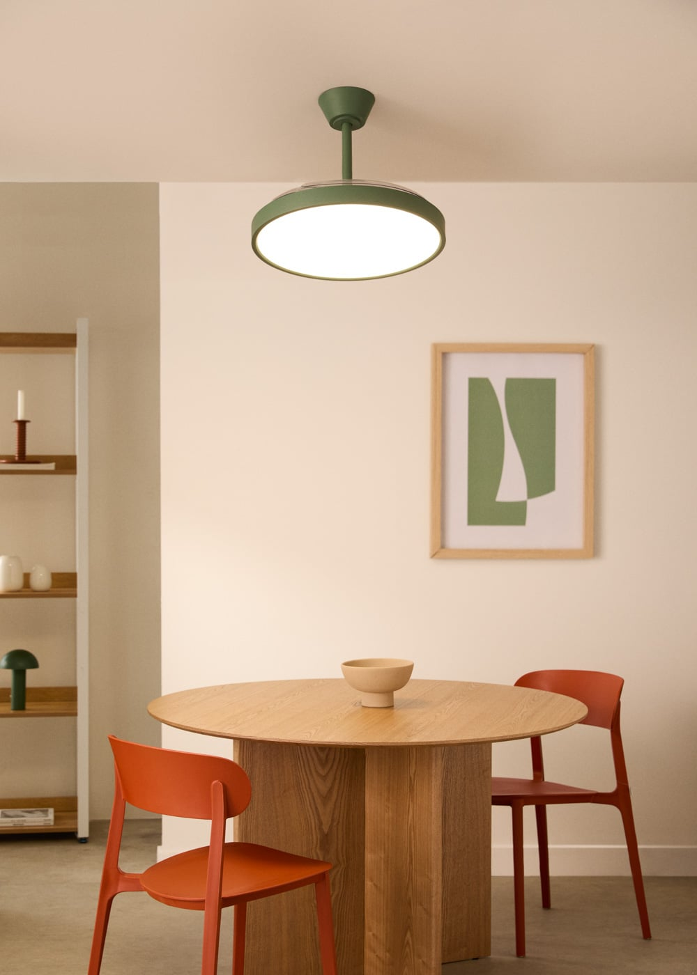 Una mesa de madera con un cuenco y dos sillas naranjas, iluminada por una lámpara de techo.