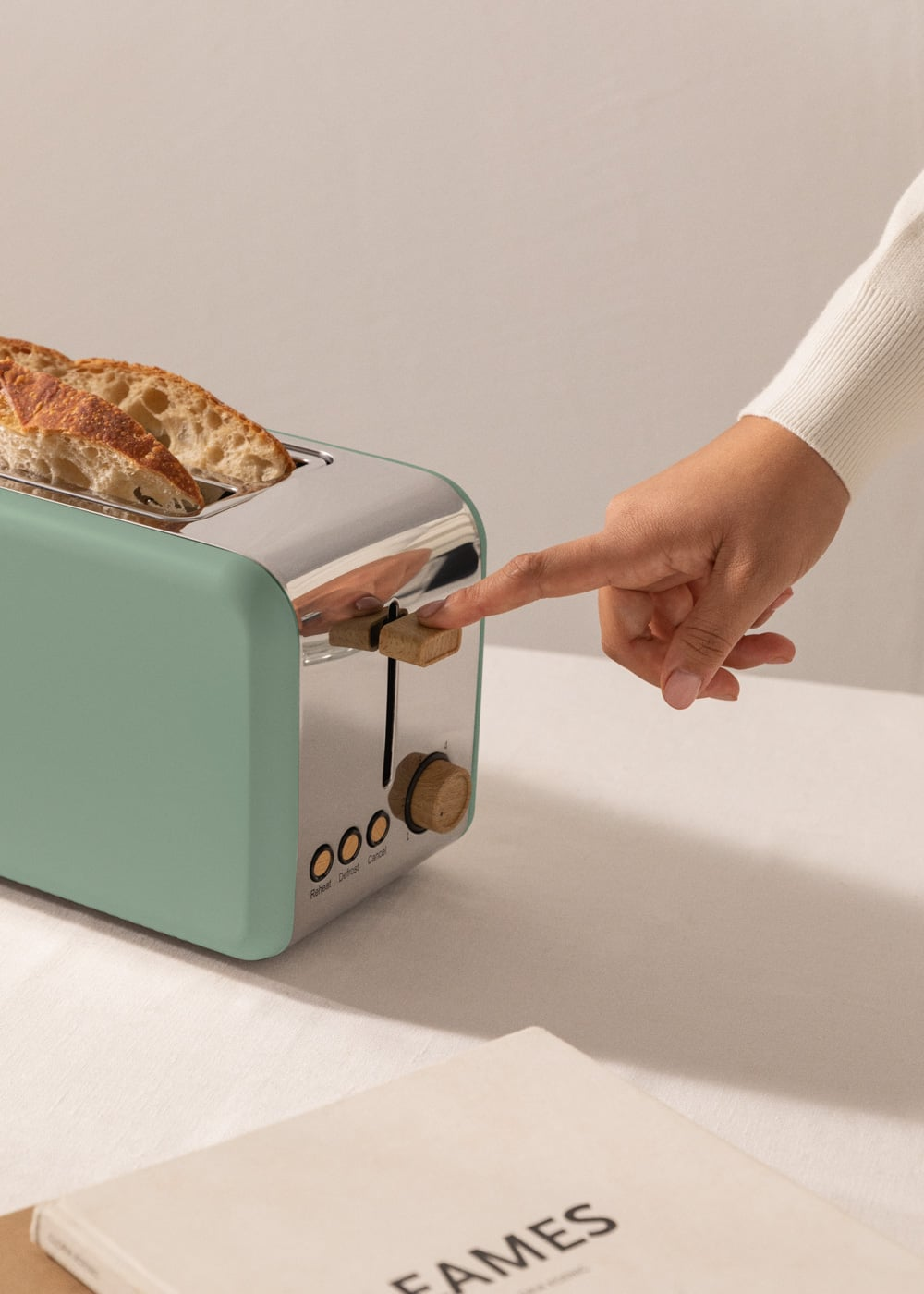 Una mano presiona la palanca de una tostadora verde menta con dos rebanadas de pan.