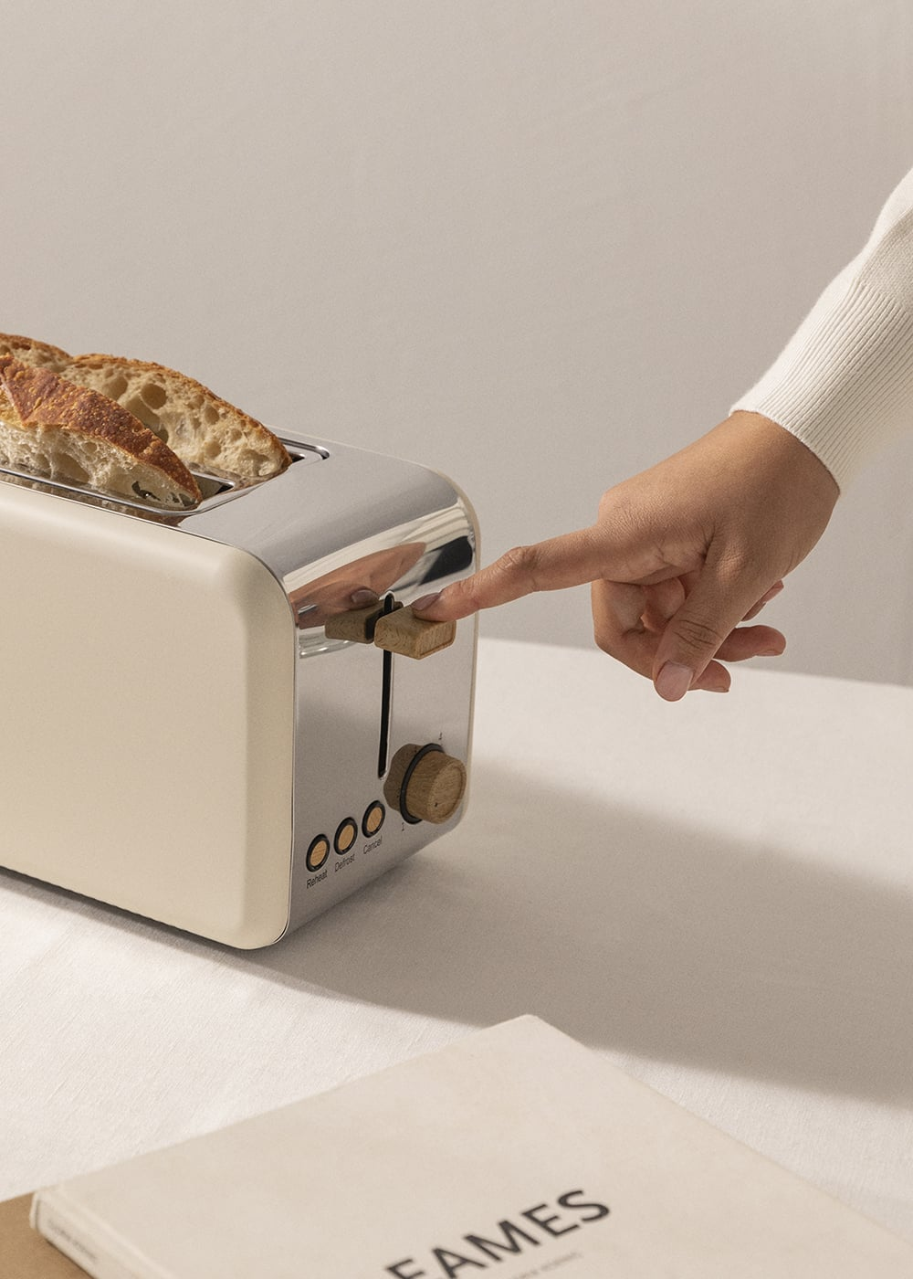 Una mano presiona la palanca de una tostadora color crema con rebanadas de pan.