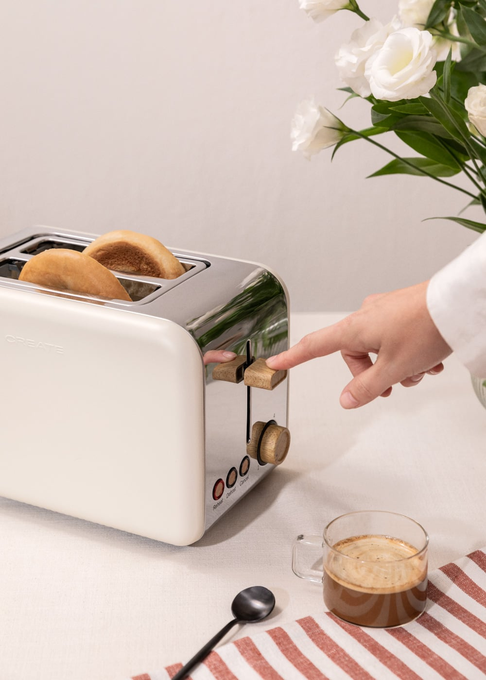 Una mano presiona la palanca de una tostadora blanca con dos panes dentro.